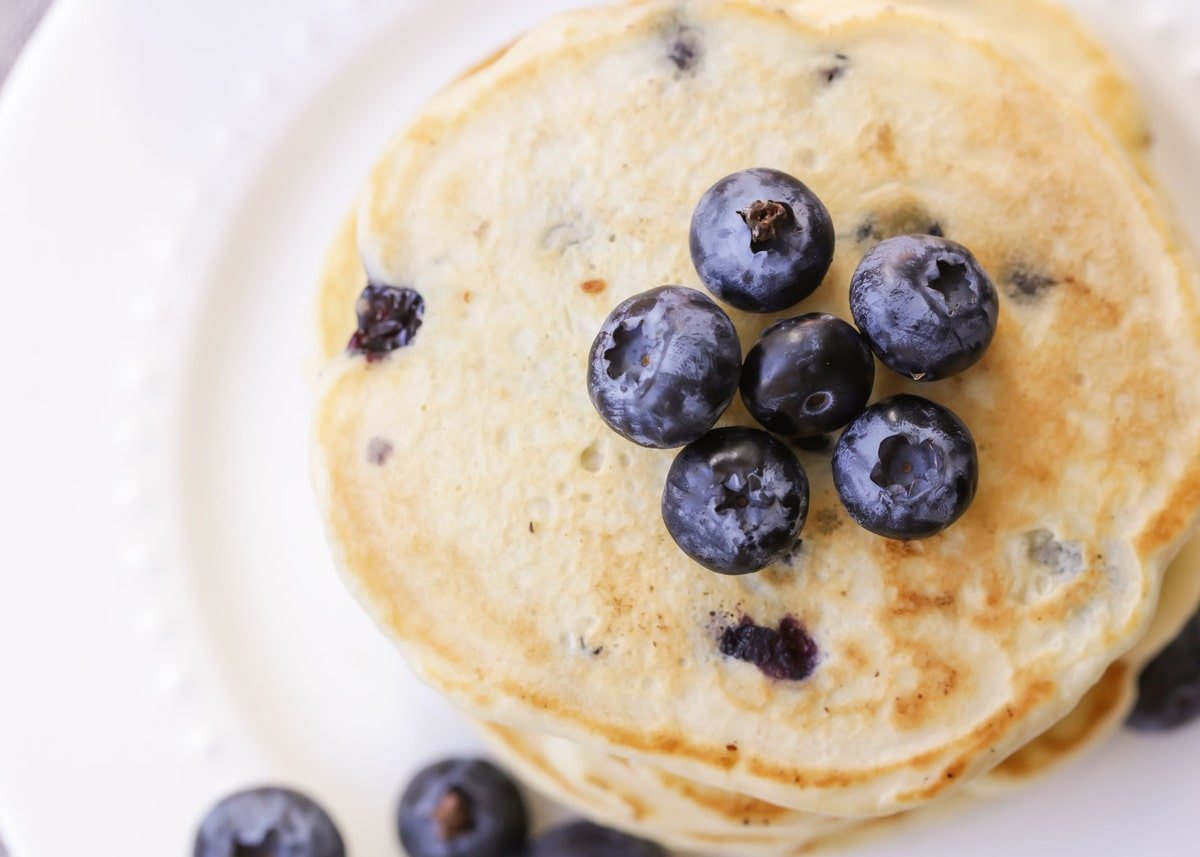 Blueberry Pancakes stacked on a white plate and topped with blueberries
