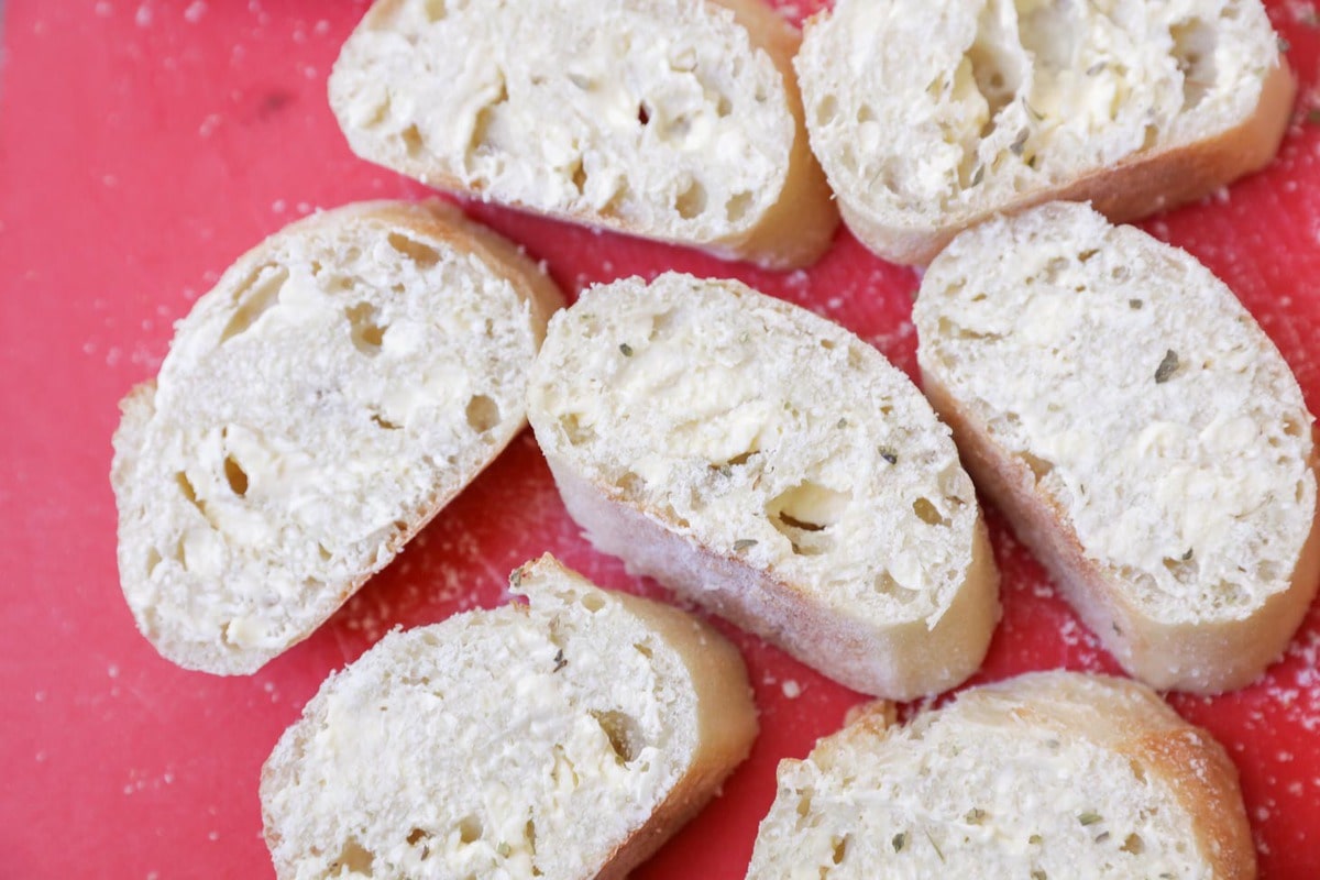 Baguette slices butter on a cutting board.