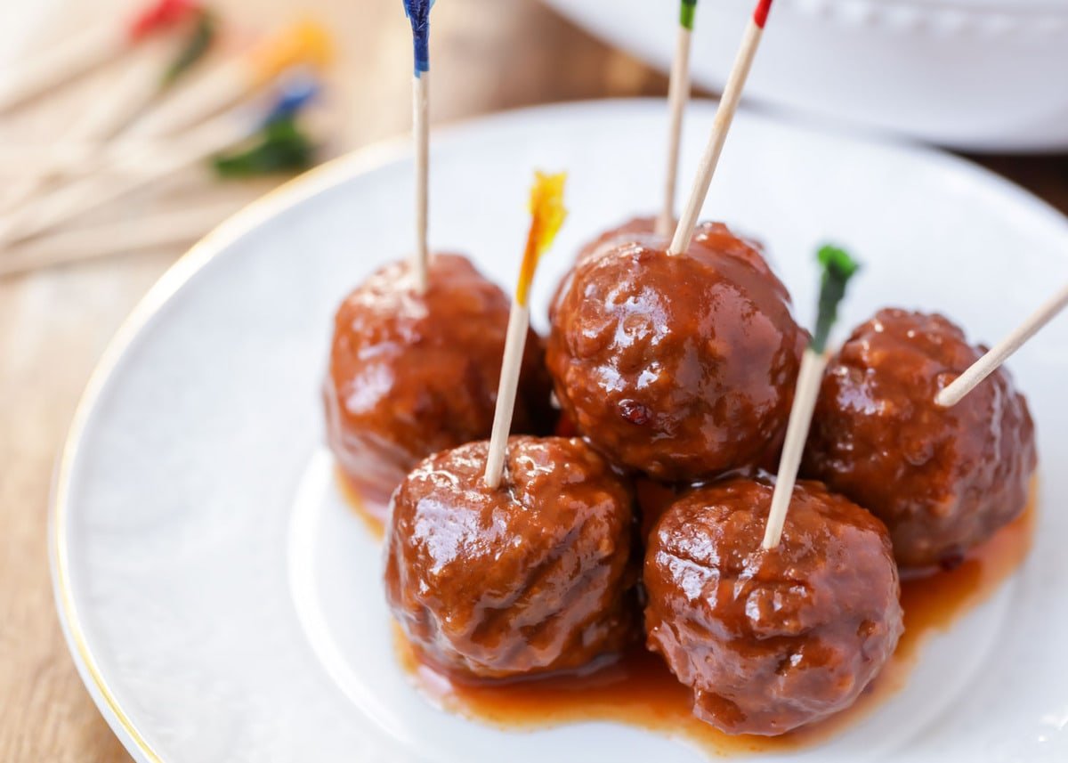 crock pot meatballs with wooden toothpicks poked into them on a white plate. 