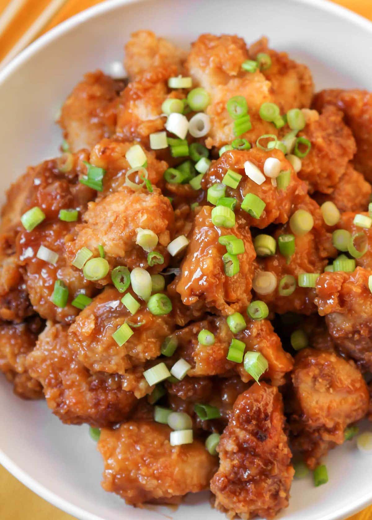 Crock Pot Orange Chicken topped with green onions in a white bowl