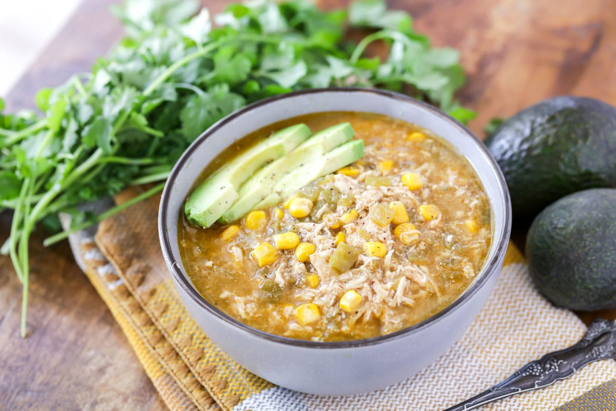 Green Chili Chicken Soup topped with avocado slices in a white bowl with a black rim. 