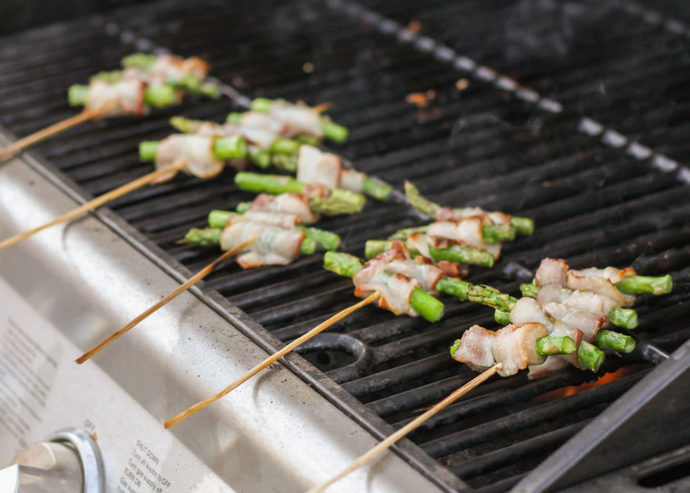 Grilling bacon wrapped asparagus skewers on an outdoor grill.