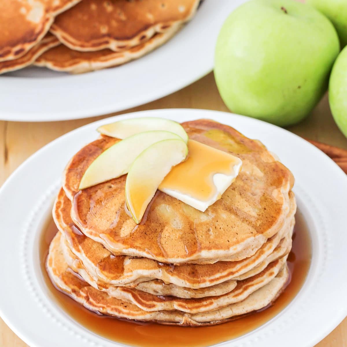 A stack of apple pancakes on a white plate covered in syrup