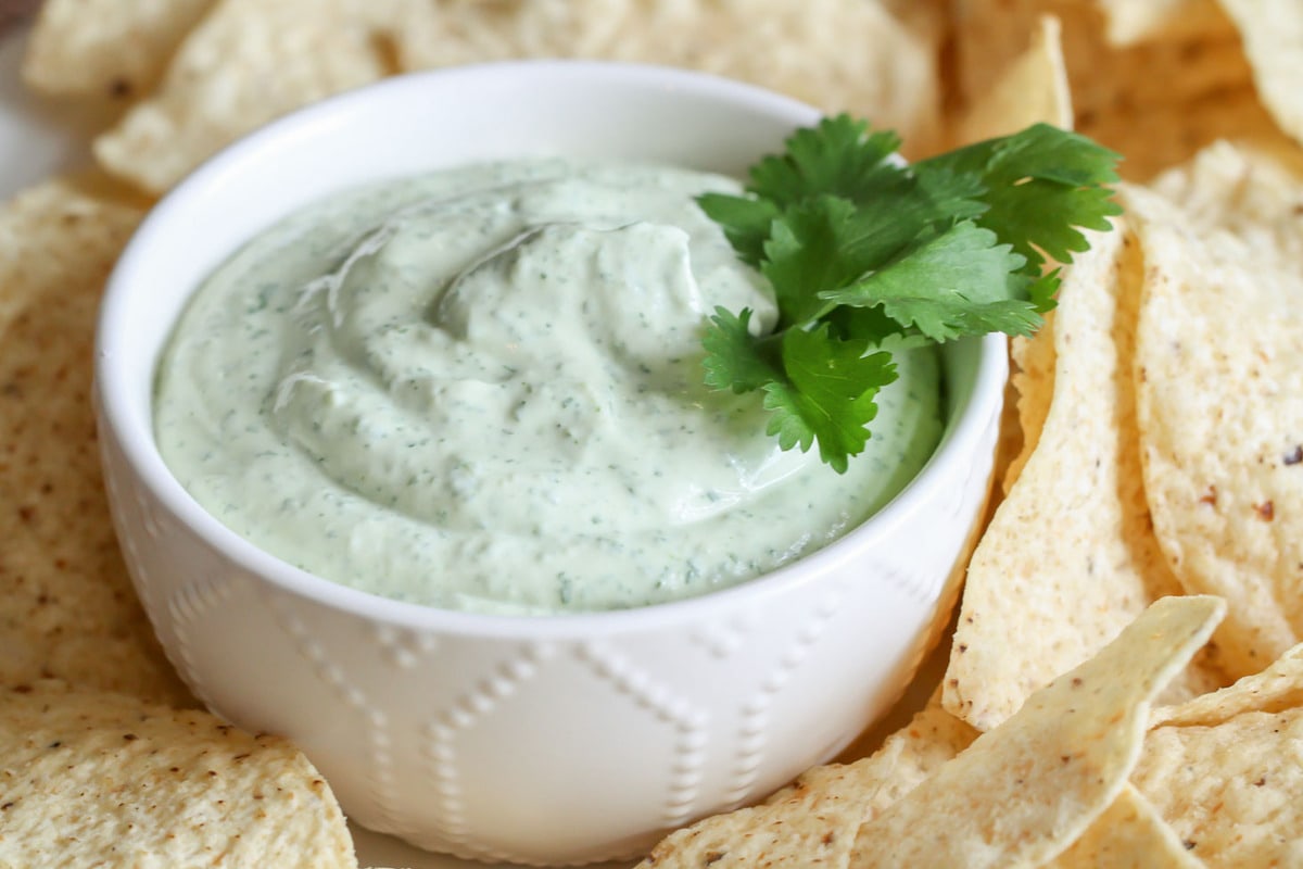 Appetizer Dips - Avocado Lime Ranch Dip in a white bowl garnished with cilantro and surrounded by tortilla chips. 