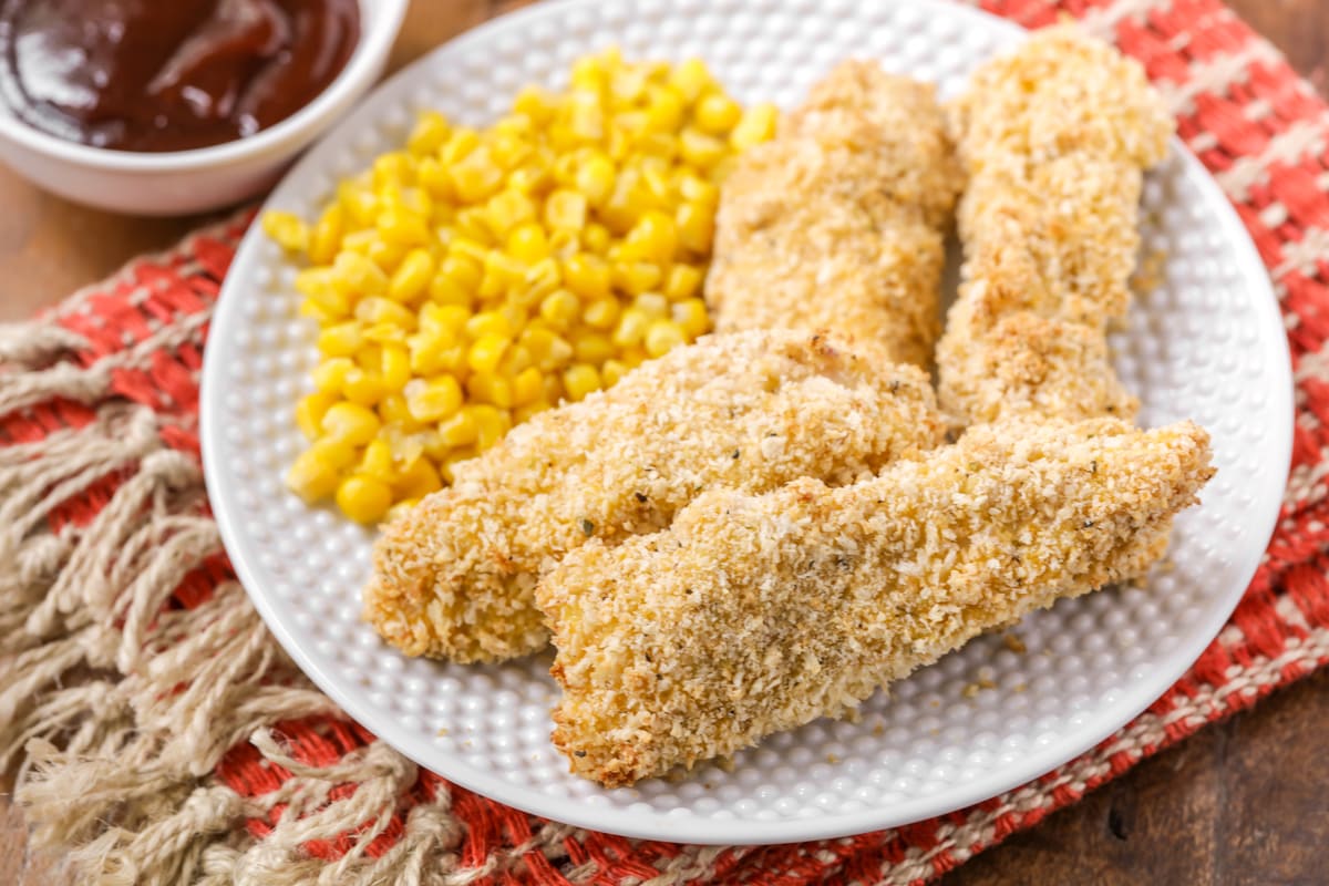 Healthy Dinner Ideas - baked chicken fingers with a side of corn on a white plate.