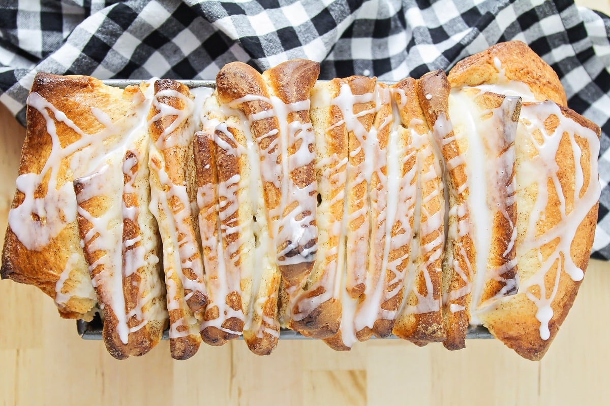 Cinnamon Roll Pull Apart Bread in a bread pan, drizzled with a glaze