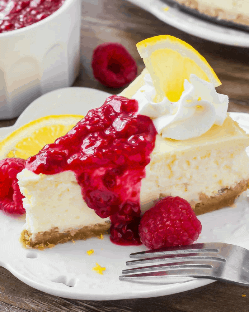 Lemon Cheesecake recipe topped with whipped cream and raspberry sauce