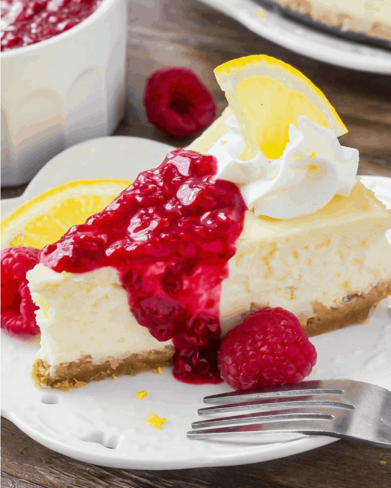 Lemon Cheesecake recipe topped with whipped cream and raspberry sauce