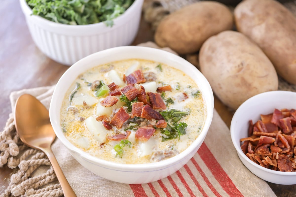 Easy soup recipes - zuppa toscana soup topped with bacon in a white bowl.