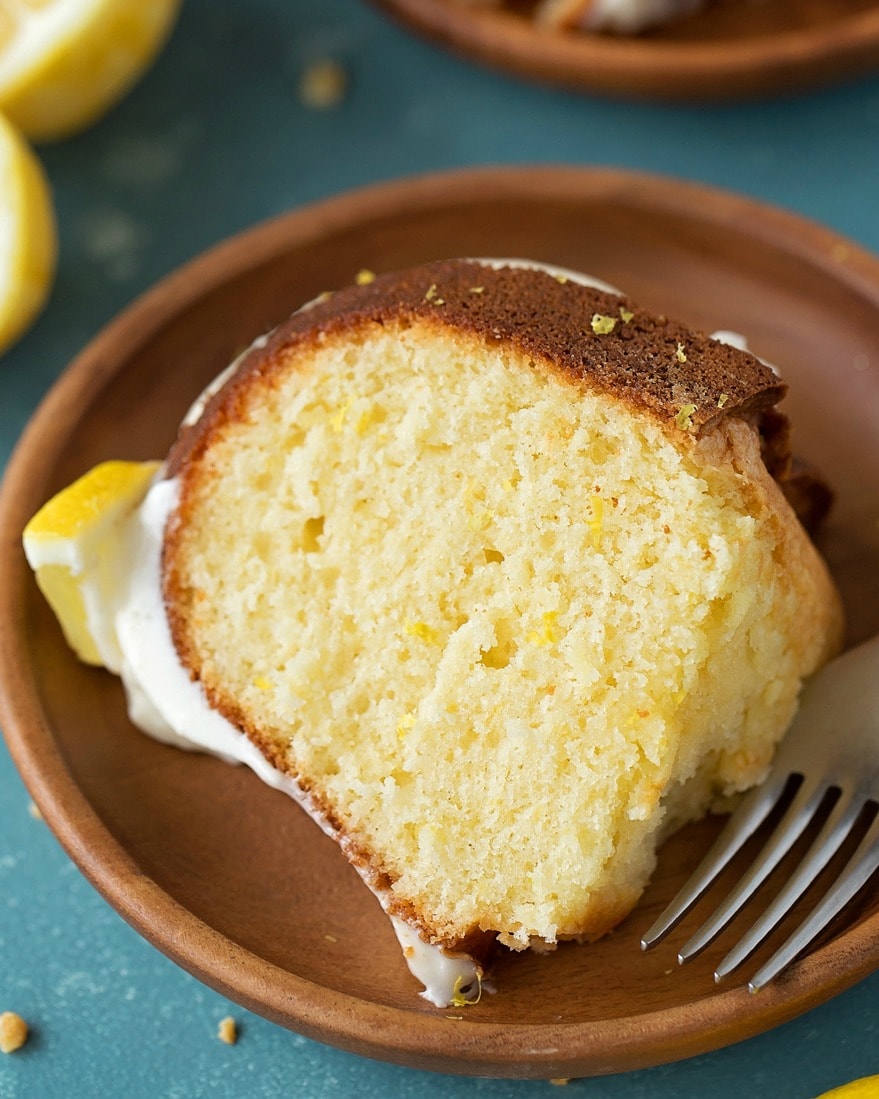 A slice of lemon bundt cake on a wooden plate with a fork resting on the plate. 