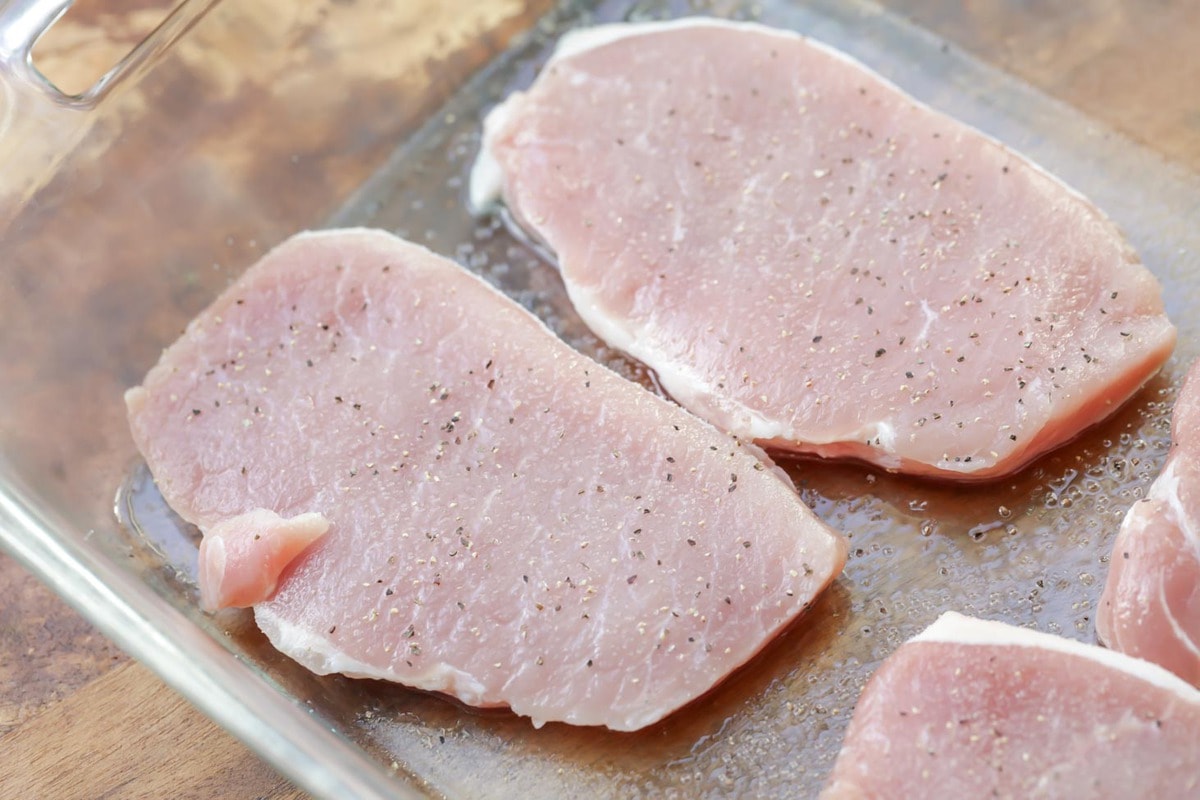 Pork chops seasoned in a glass baking dish.