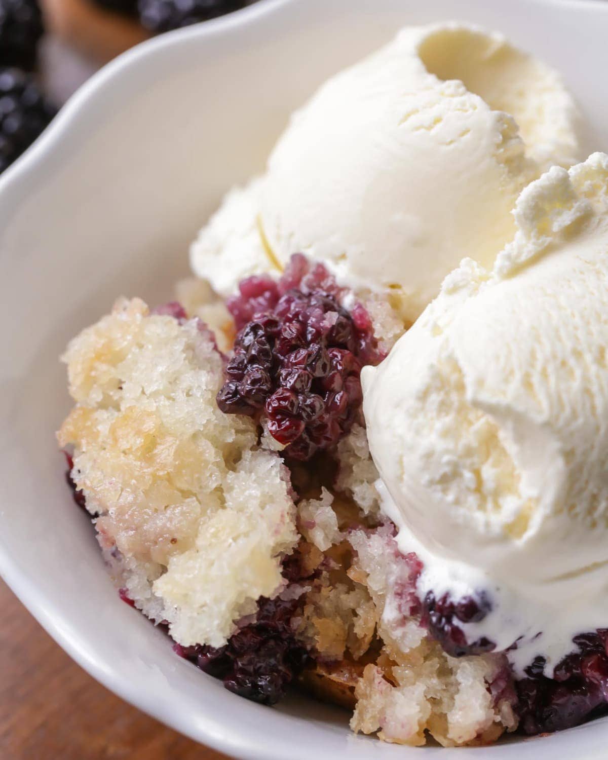 Blackberry cobbler in a bowl with two scoops of vanilla icecream