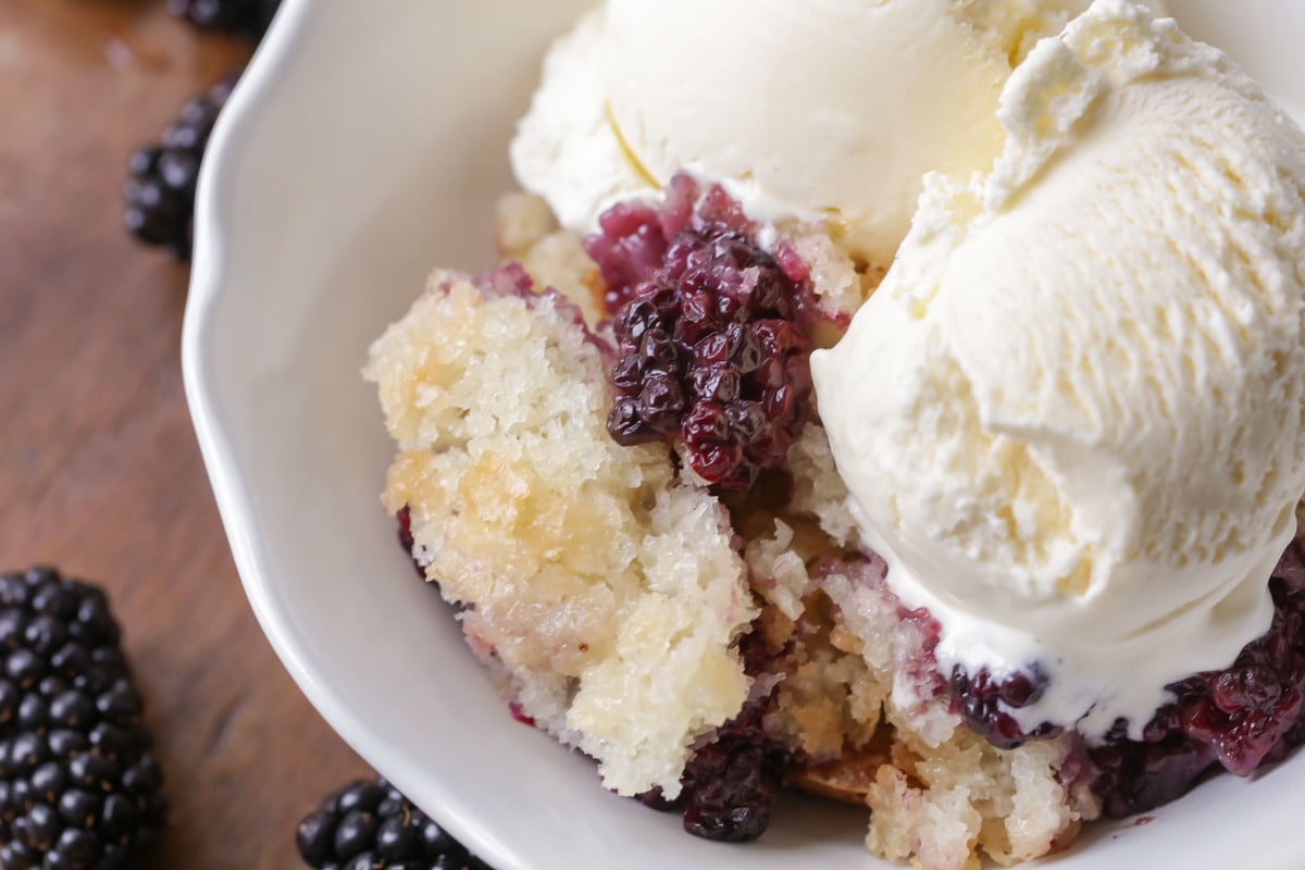 Easy Blackberry Cobbler topped with two scoops of vanilla ice cream in a white bowl.