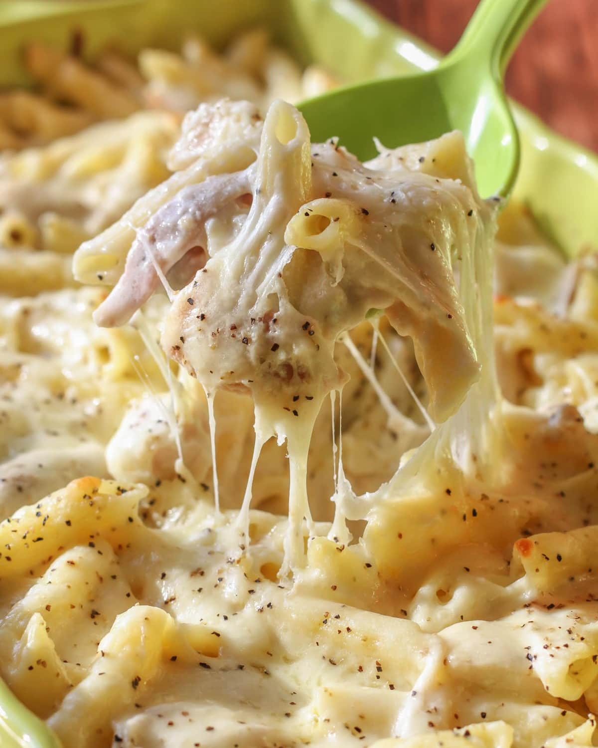 Scooping chicken alfredo bake from a baking dish.