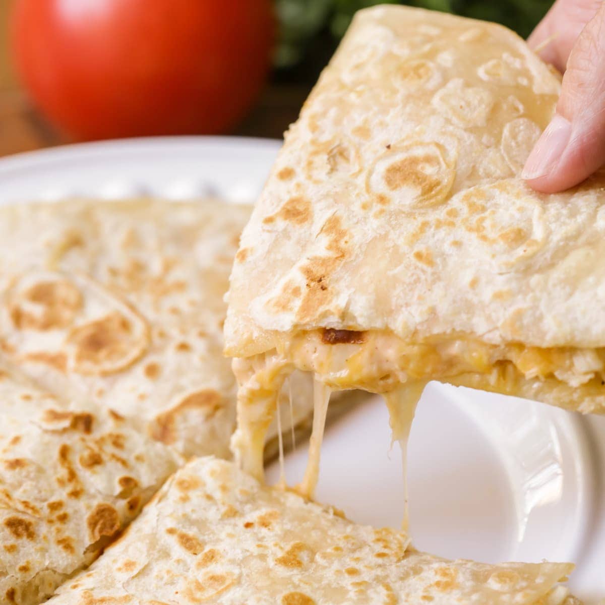 A hand holding a slice of Chicken Quesadilla.