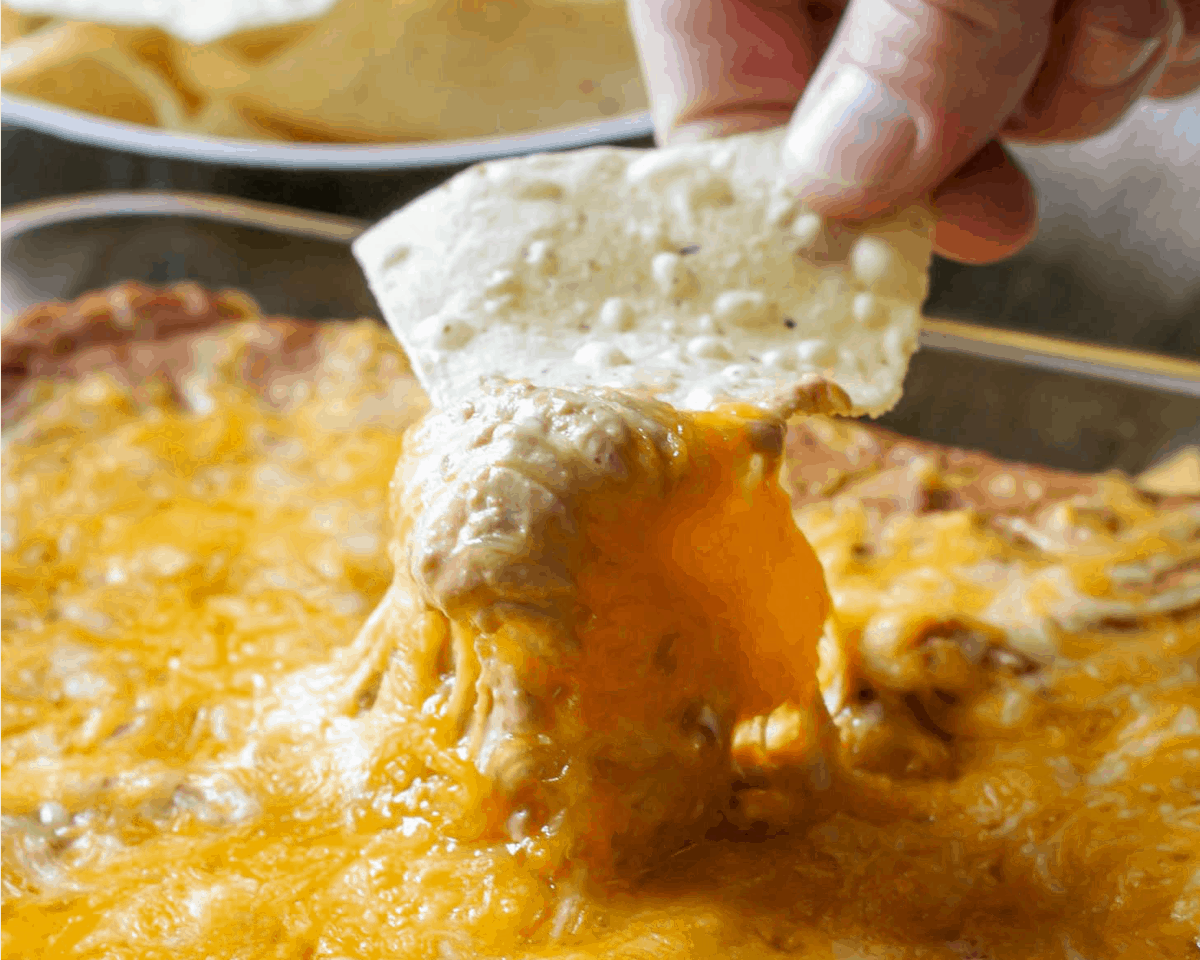 Appetizer Dips - A tortilla chip being dipped into cream cheese bean dip.