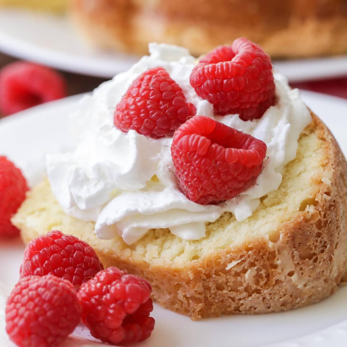 A slice of homemade cream cheese Pound Cake topped with whipped cream and raspberries.