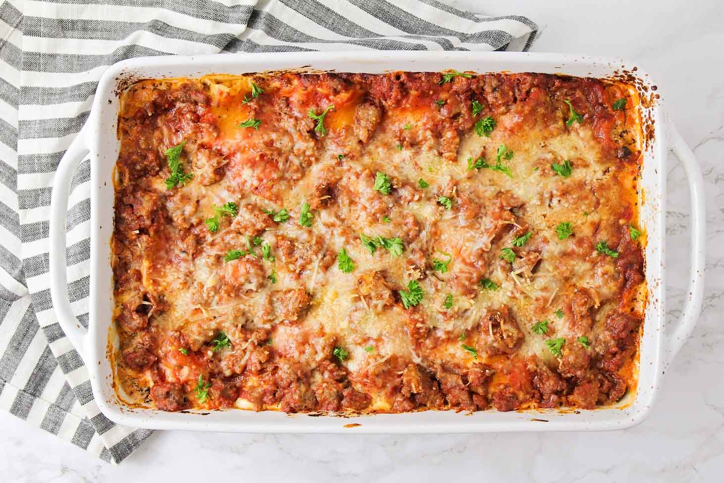 Sunday Dinner Ideas - Easy lasagna recipe served in a white casserole dish topped with fresh herbs.
