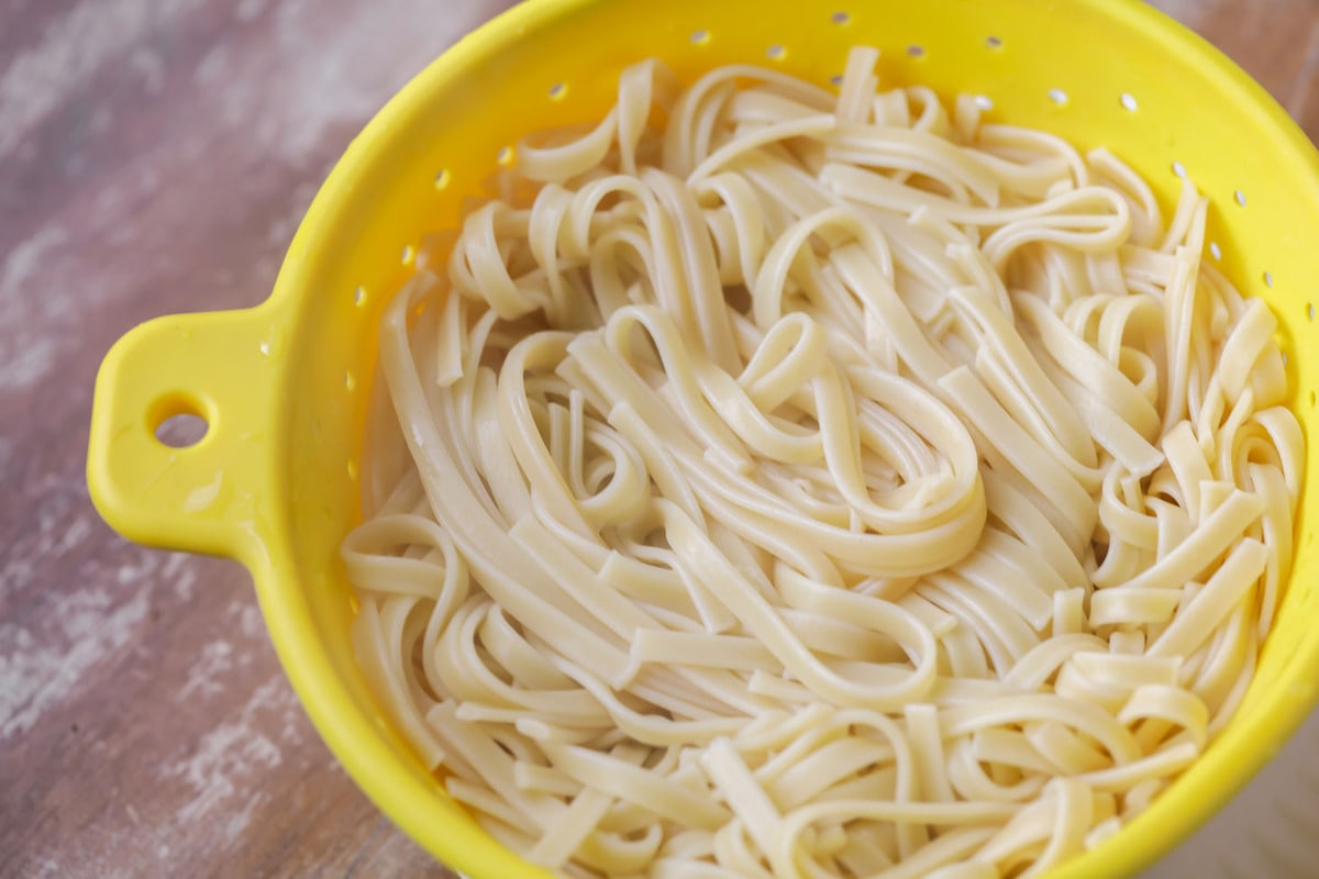 Fettuccine Noodles draining in a yellow colander.