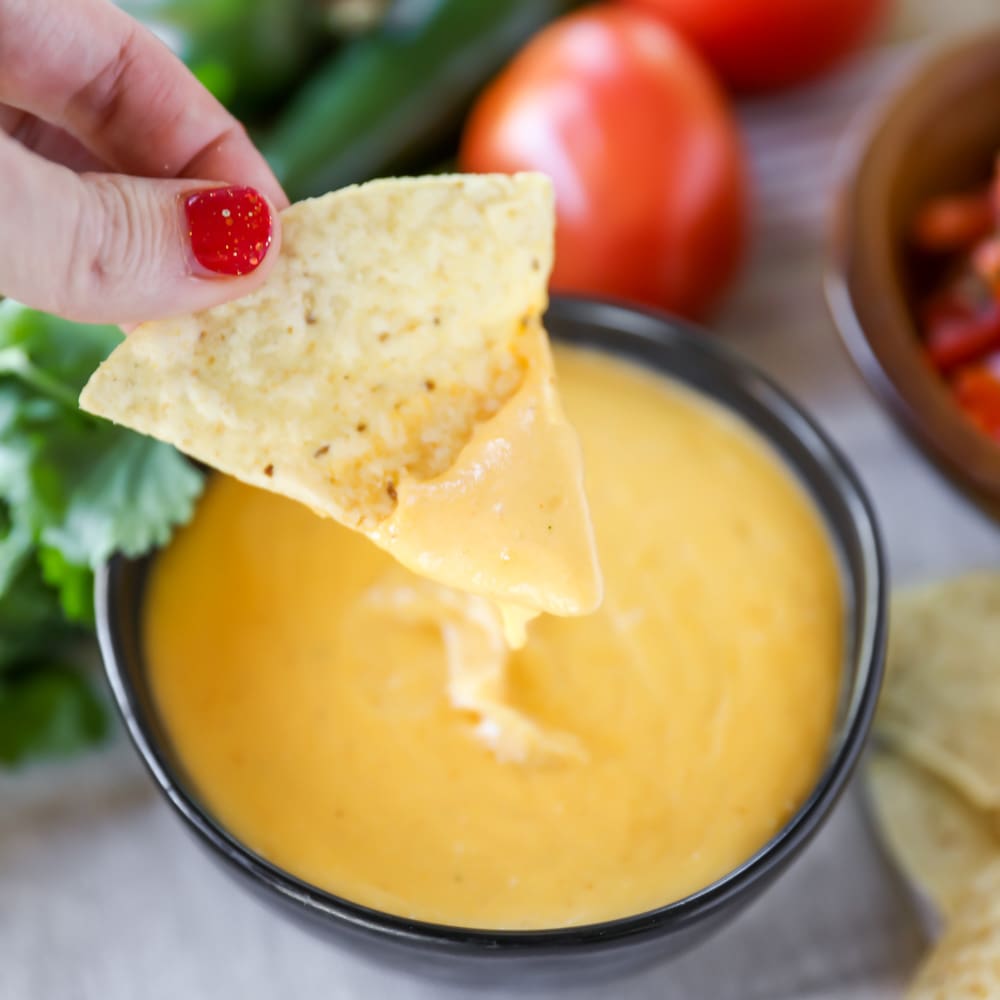 A hand dipping a chip into nacho cheese sauce