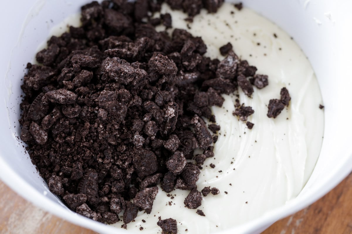 Adding crushed oreos to fudge mixture in a white mixing bowl.