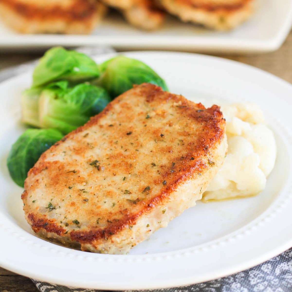 Baked Parmesan Pork Chop on a plate with mashed potatoes and brussel sprouts