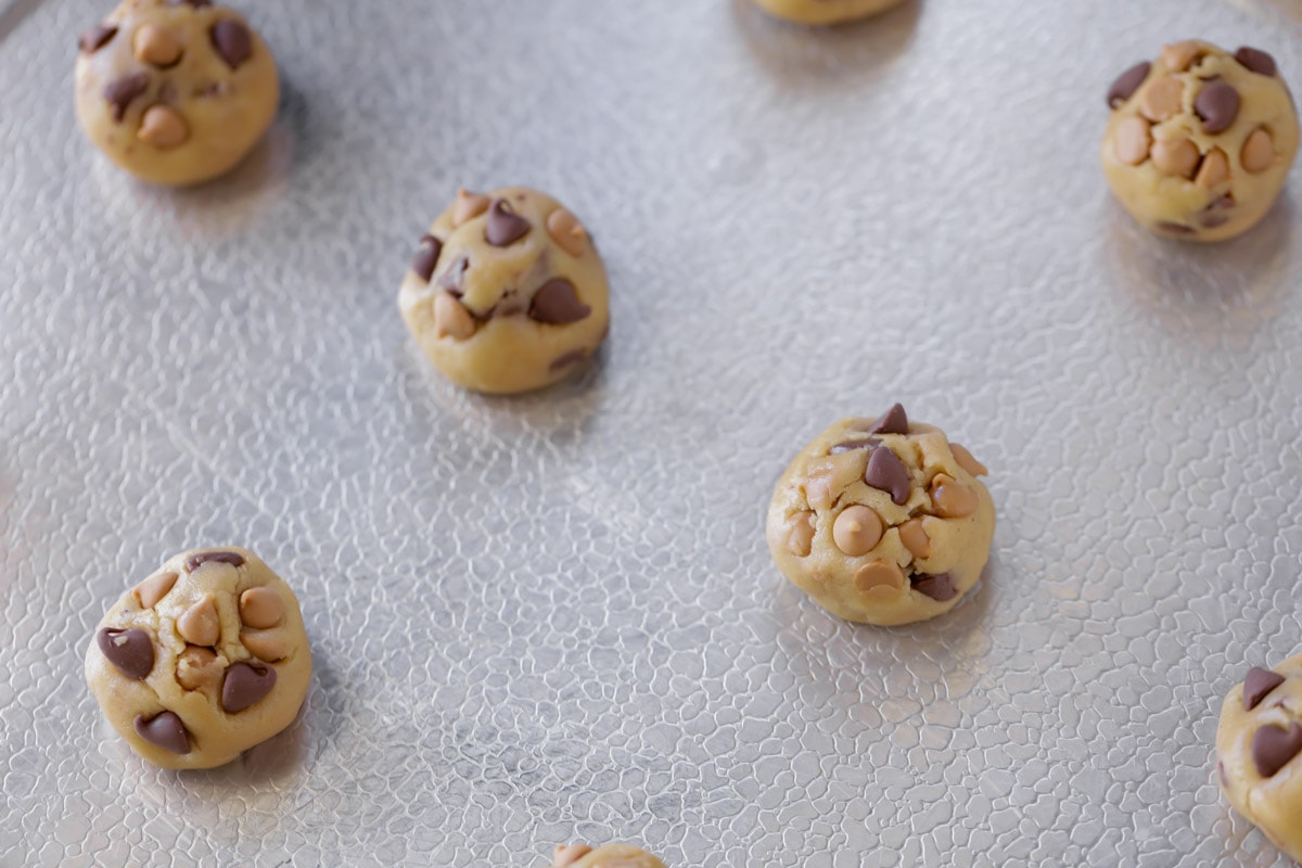 Balls of cookie dough with chips on a cookie sheet