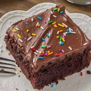 A square slice of moist sour cream chocolate cake served on a white plate.