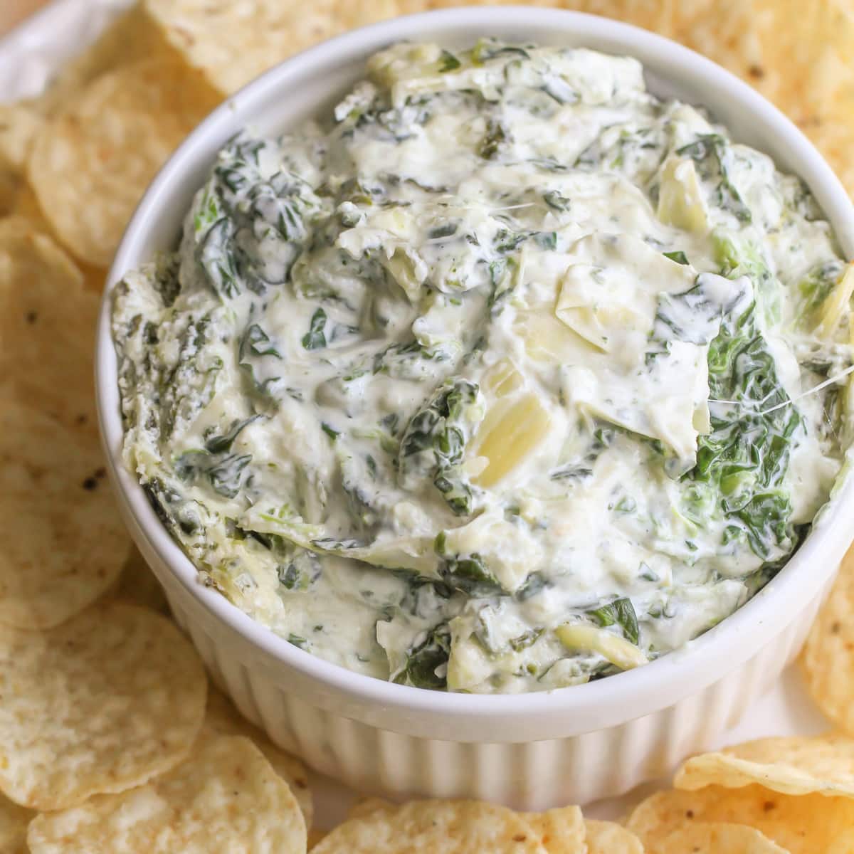 Easy Appetizers - Spinach Artichoke Dip in a white ramekin surrounded by round tortilla chips on a white plate. 