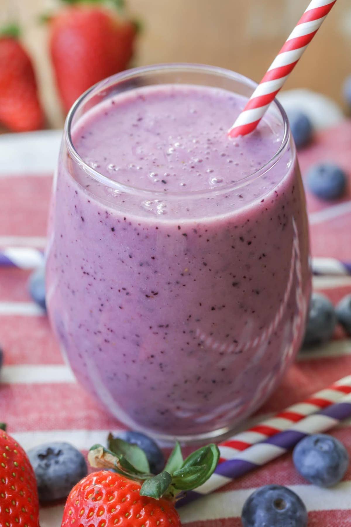Strawberry and Blueberry Smoothies in a glass served with a red and white straw.