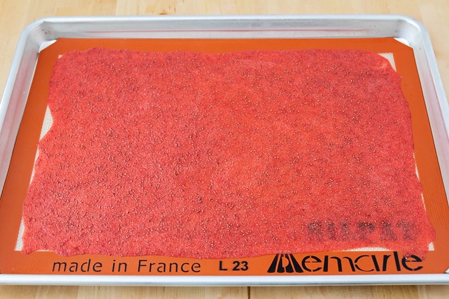 Strawberry puree spread on a baking sheet and silicone mat for fruit leather recipe.