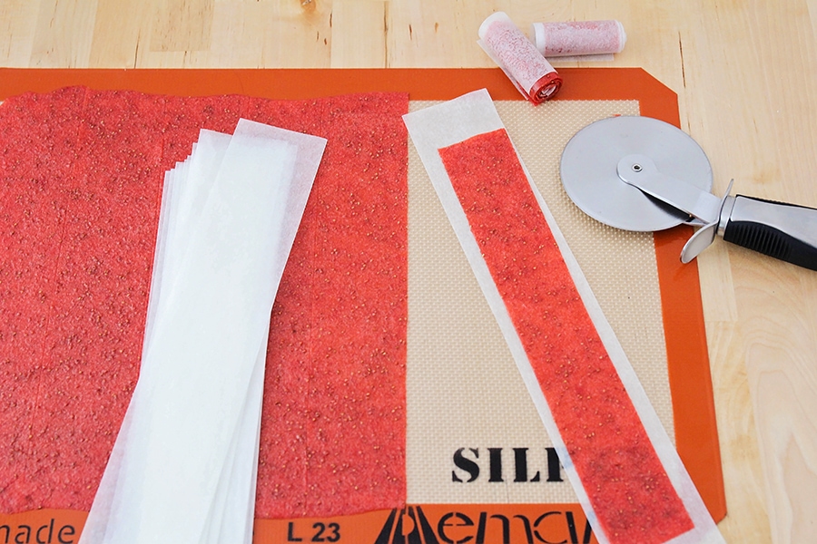 Cut strips of fruit puree on strips of parchment paper for making fruit leather recipe.