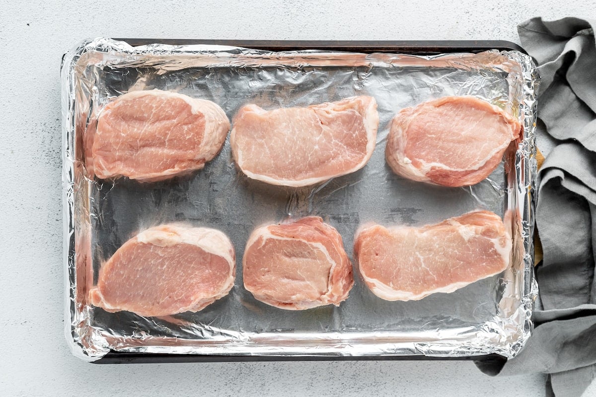 Overhead view of raw pork chops resting on a foil-lined baking sheet.