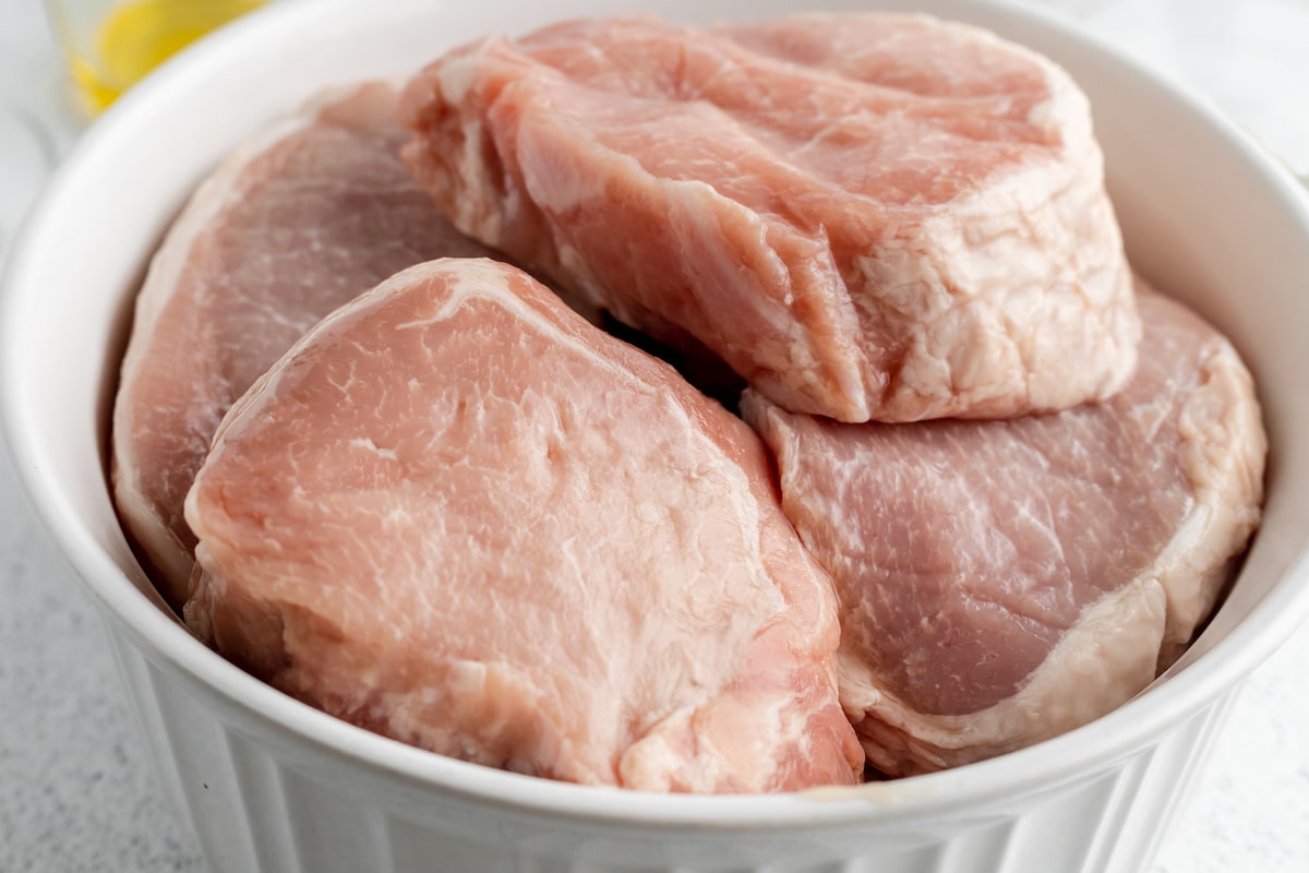 Raw pork chops in a round white dish.
