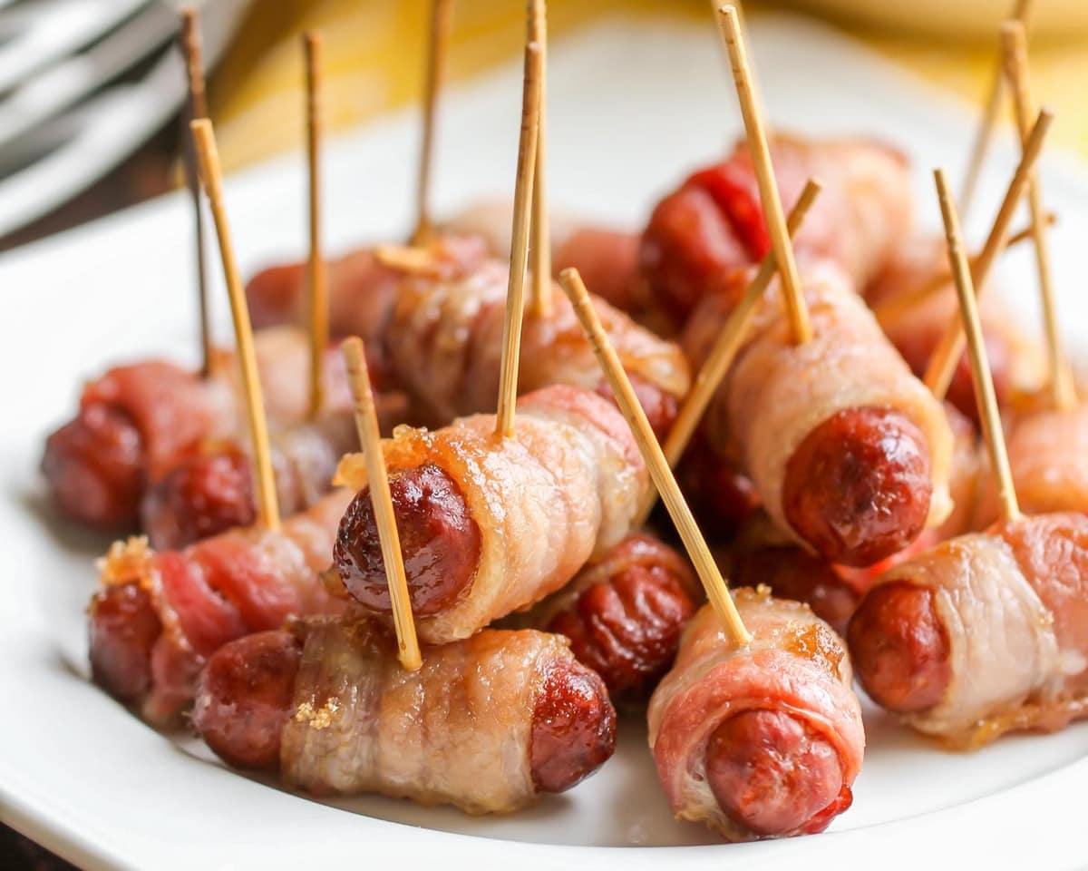 Bacon Wrapped Smokies on a white plate stuck with toothpicks.