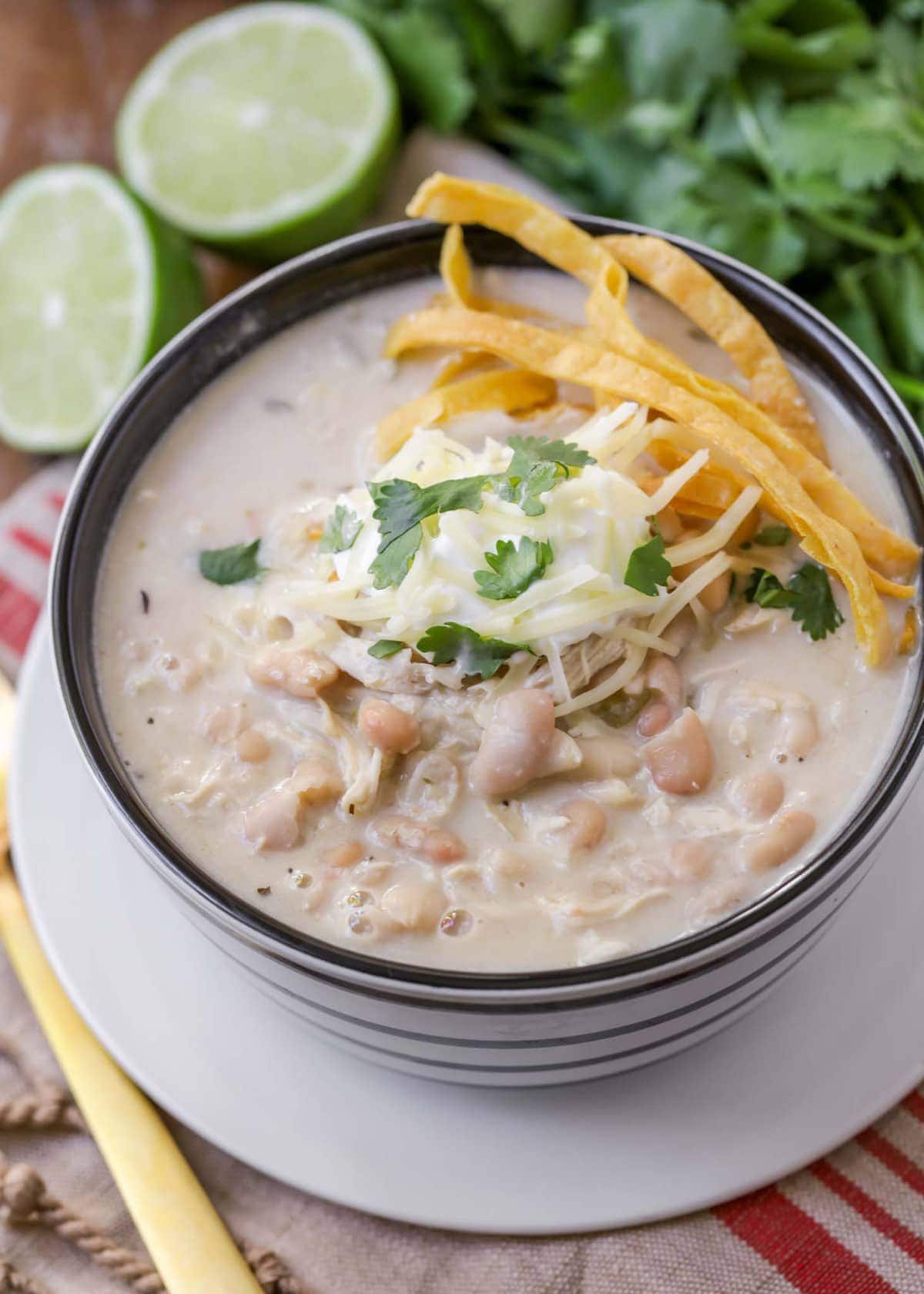 White Chicken Chili in bowl topped with shredded cheese, tortilla strips, and cilantro.
