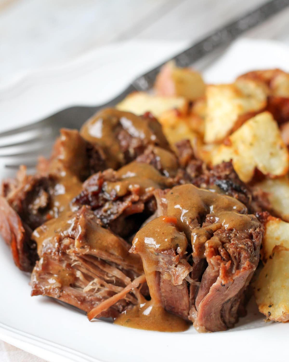 Close up of pot roast recipe and potatoes served on a white plate.