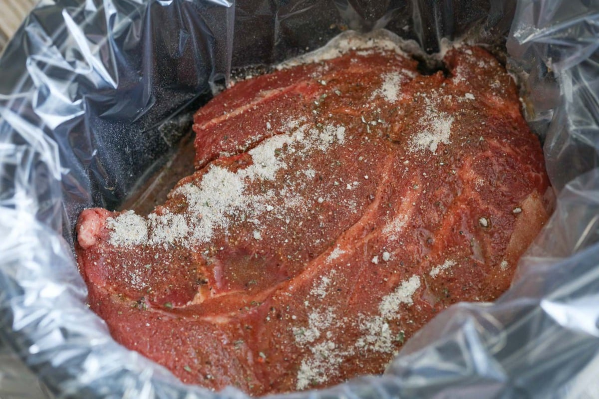 Seasoned pot roast in a lined crock pot.