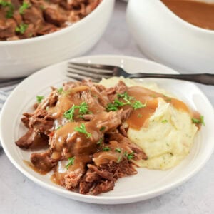 Crock pot pot roast recipe on plate with mashed potatoes and gravy.