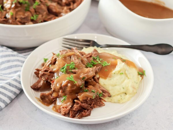 Crock pot pot roast recipe on plate with mashed potatoes and gravy.