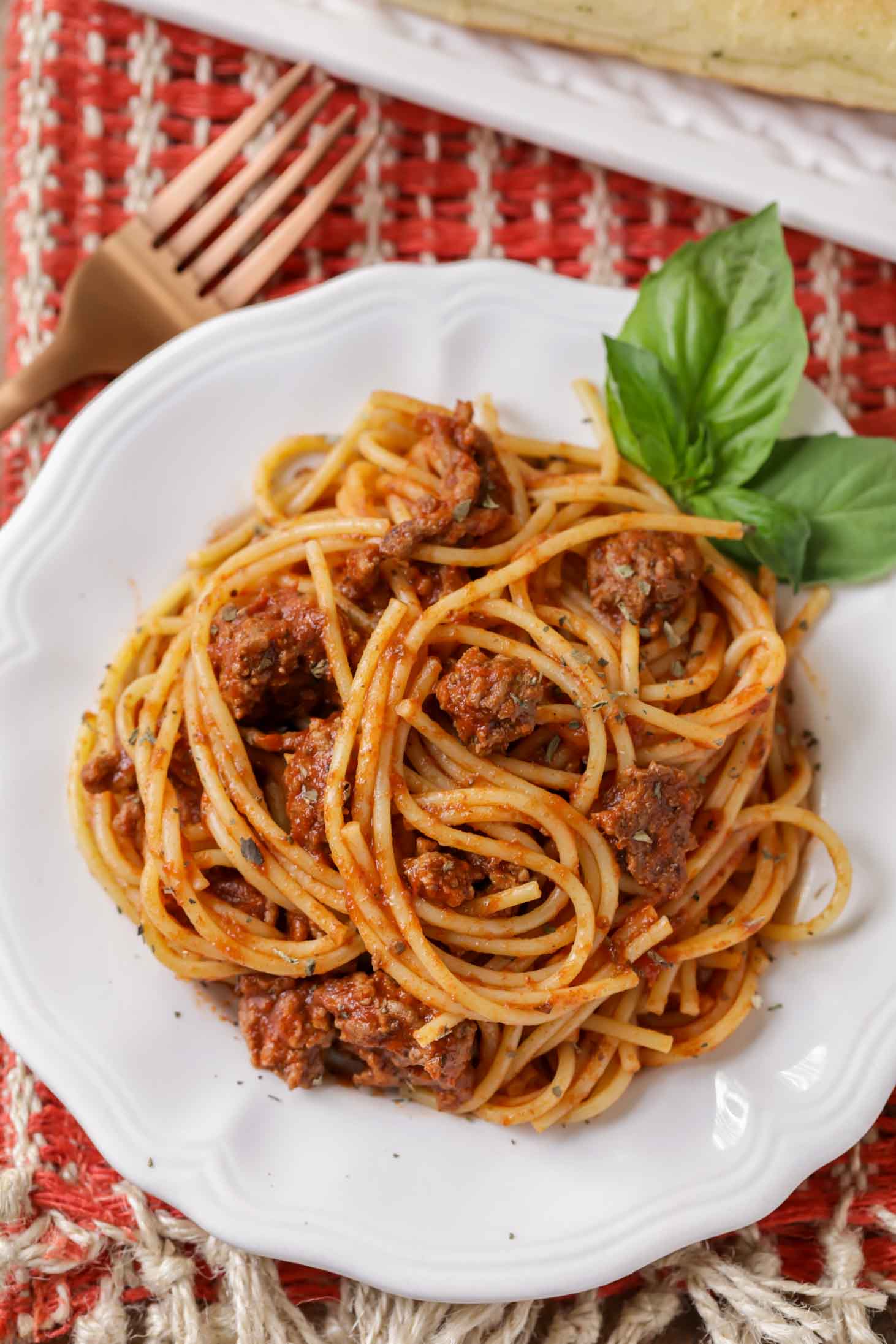 Spaghetti served on a white plate with fresh basil.