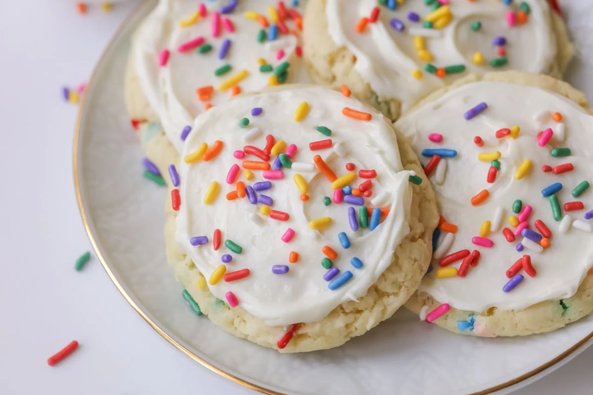 Funfetti Cookies covered in frosting and sprinkles on a white plate.