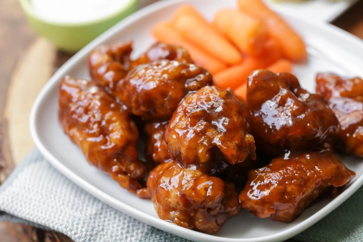 Super Bowl Appetizers - boneless honey BBQ wings  with a side of baby carrots on a white plate.