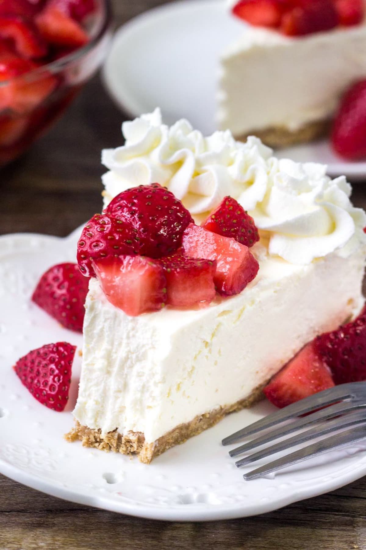 A close up of a slice of cheesecake topped with strawberries and a bite missing.