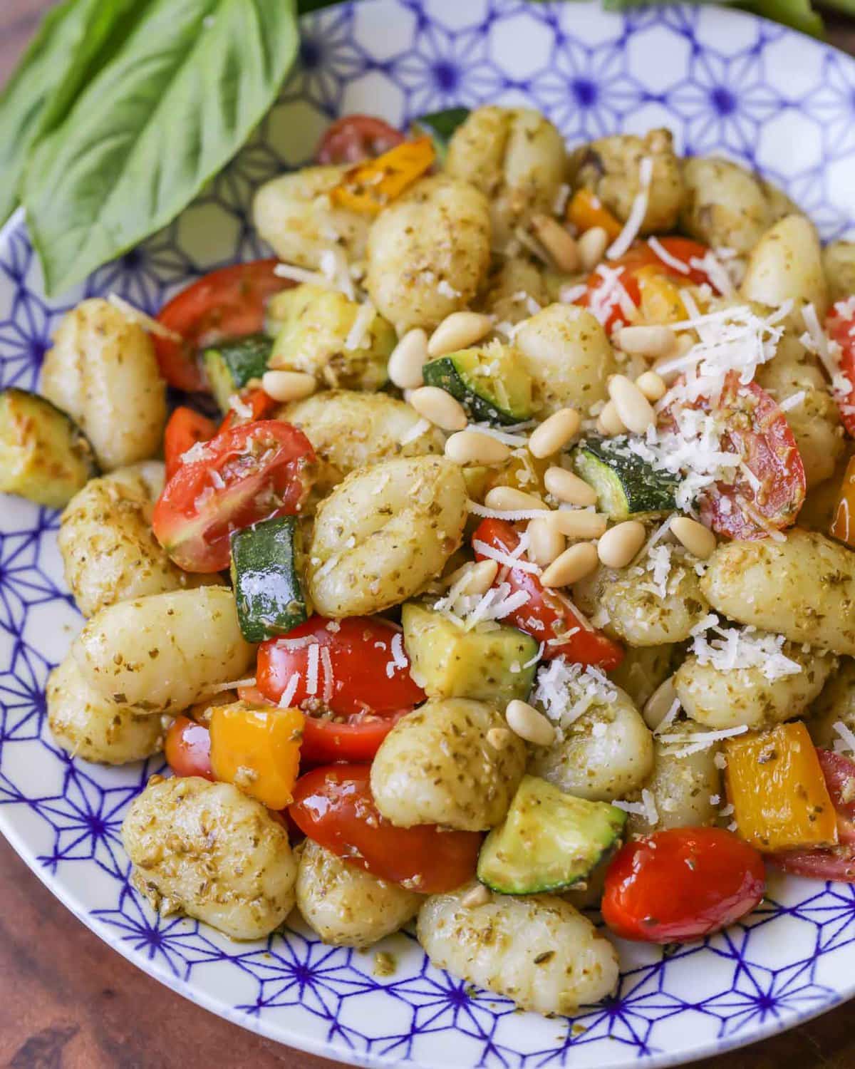 Pesto Gnocchi garnished with parmesan and pine nuts in a blue and white bowl.