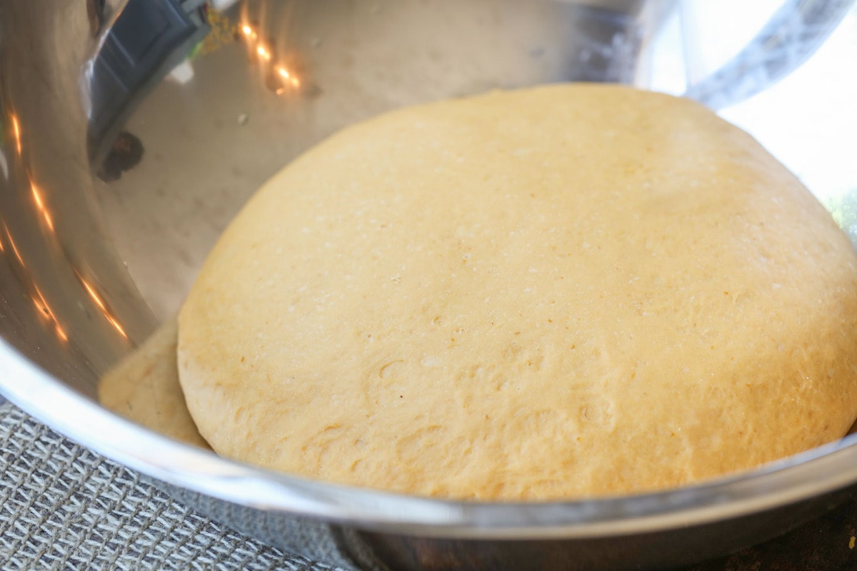 Pumpkin cinnamon roll dough rising in a metal bowl.