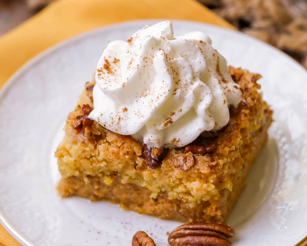Pumpkin Recipes - Pumpkin Dump Cake topped with pecans and whipped cream on a white plate.
