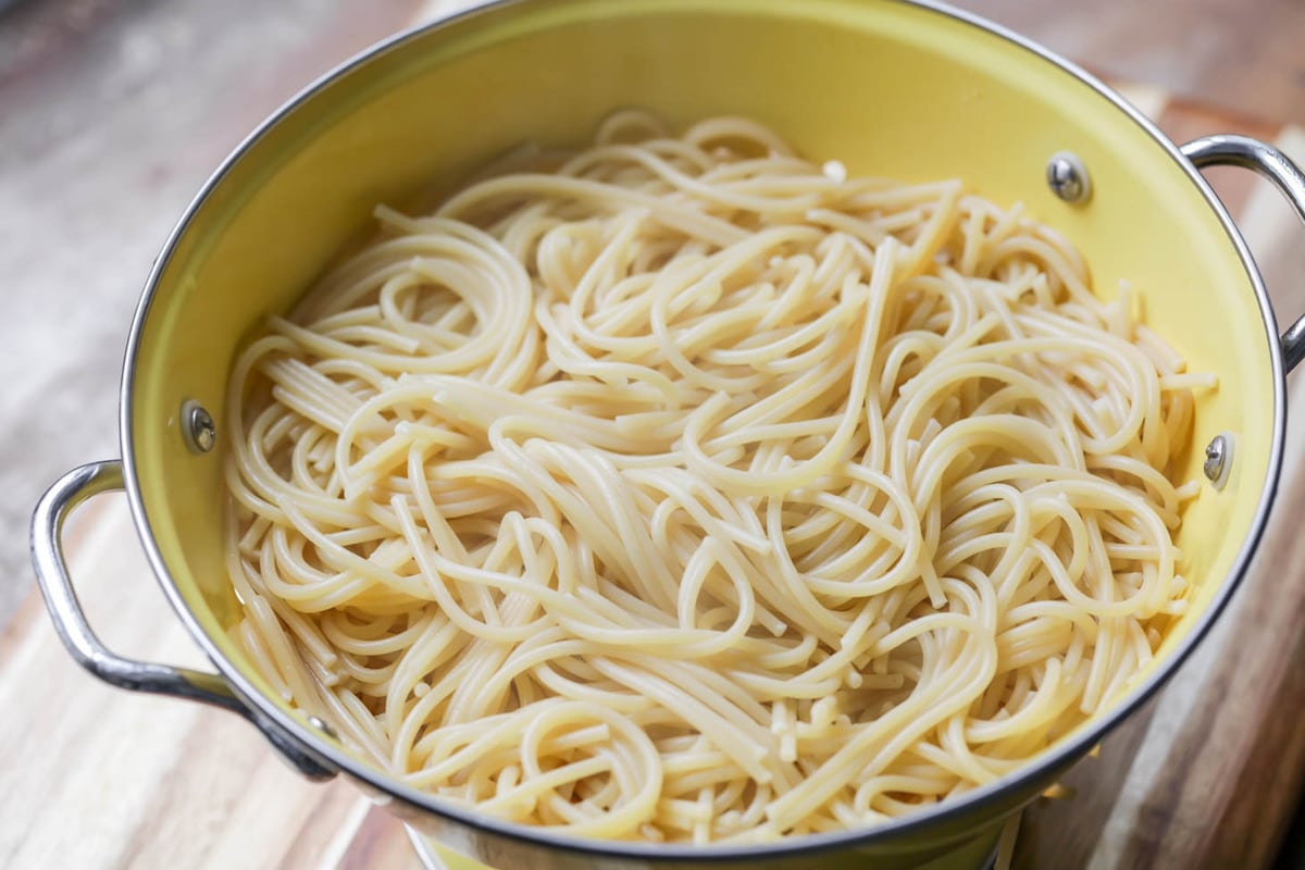 Cooked spaghetti in a yellow colander.