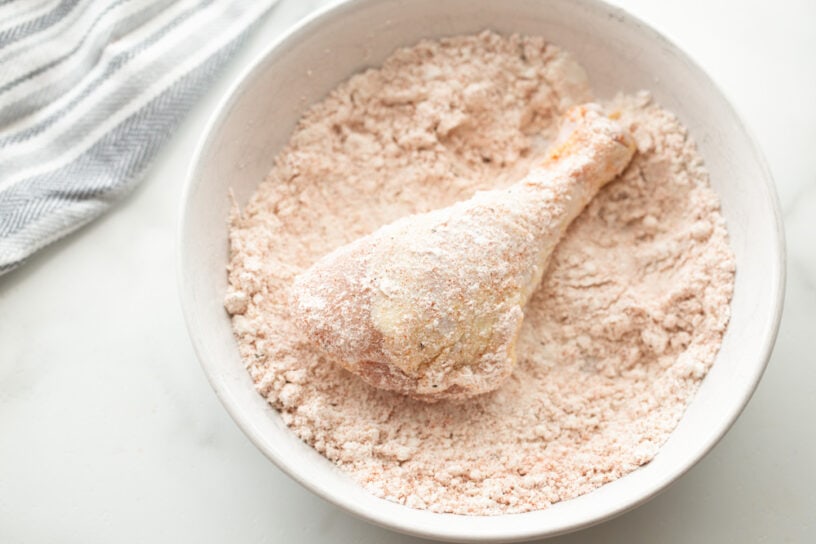 Chicken leg in a bowl of flour.