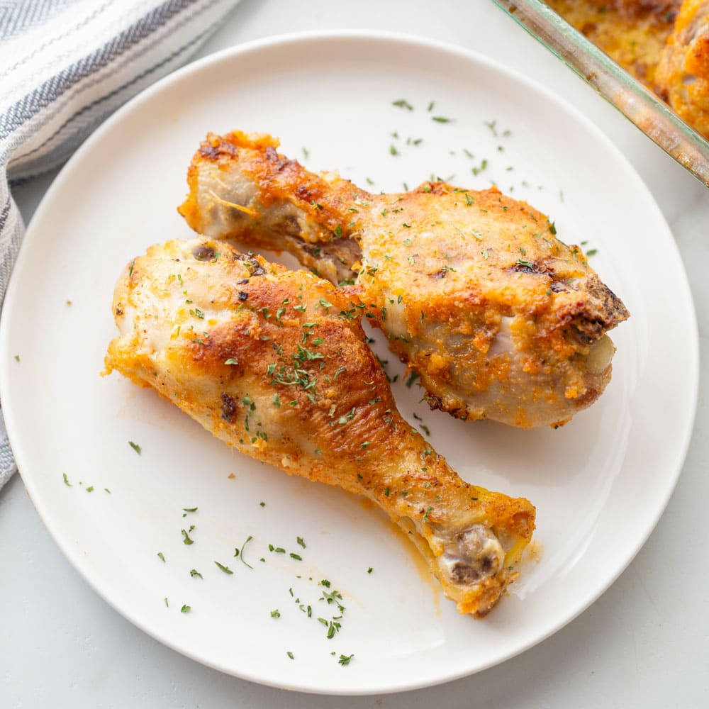 Two baked drumsticks in oven on a white plate.